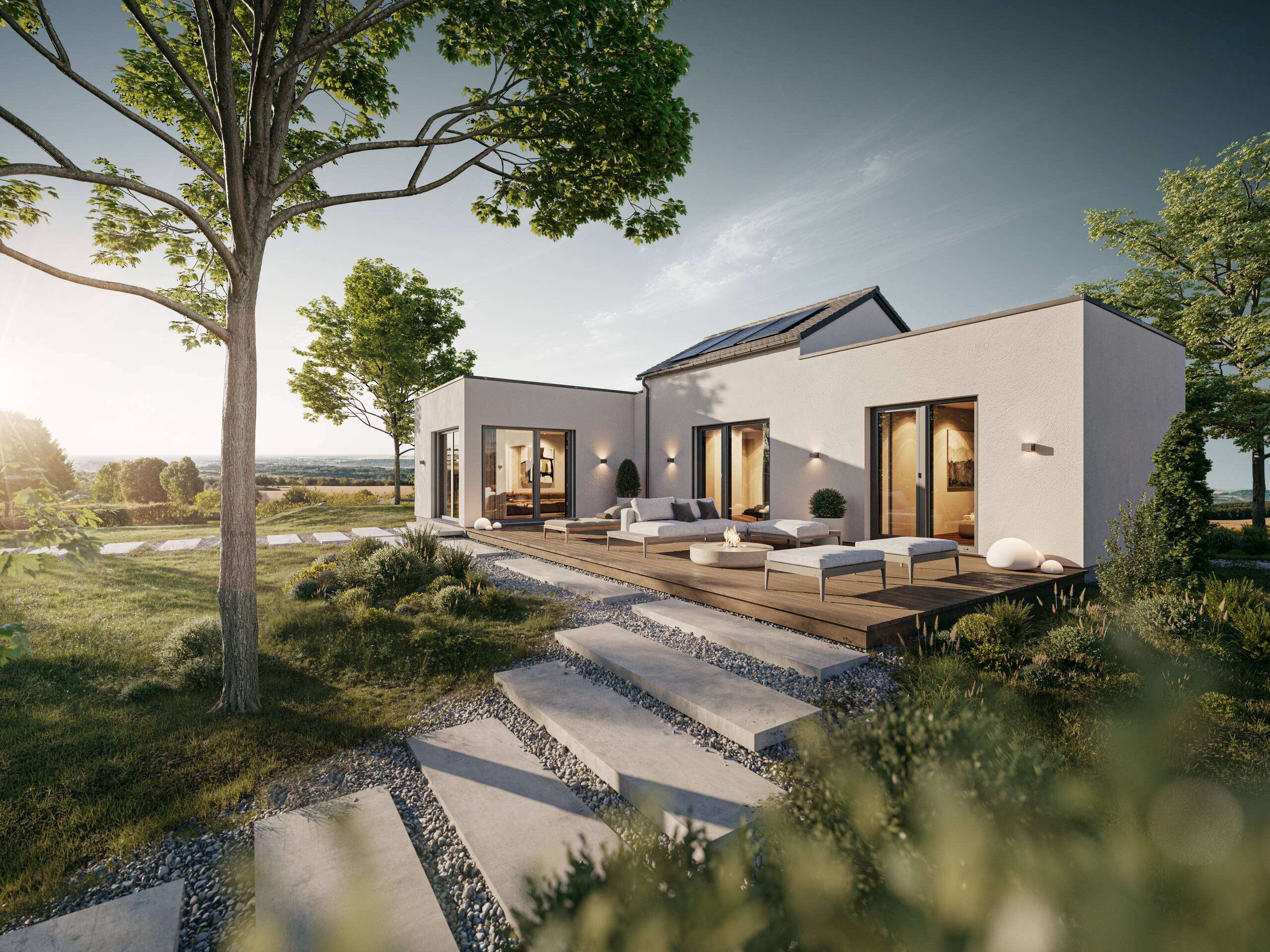 Ein modernes, helles Haus mit großen Fenstern und einer Holzterrasse. Die Umgebung ist grün mit einem gepflegten Garten, auf dem Steinstufen zu sehen sind. Im Hintergrund leuchtet die Sonne über sanften Hügeln.