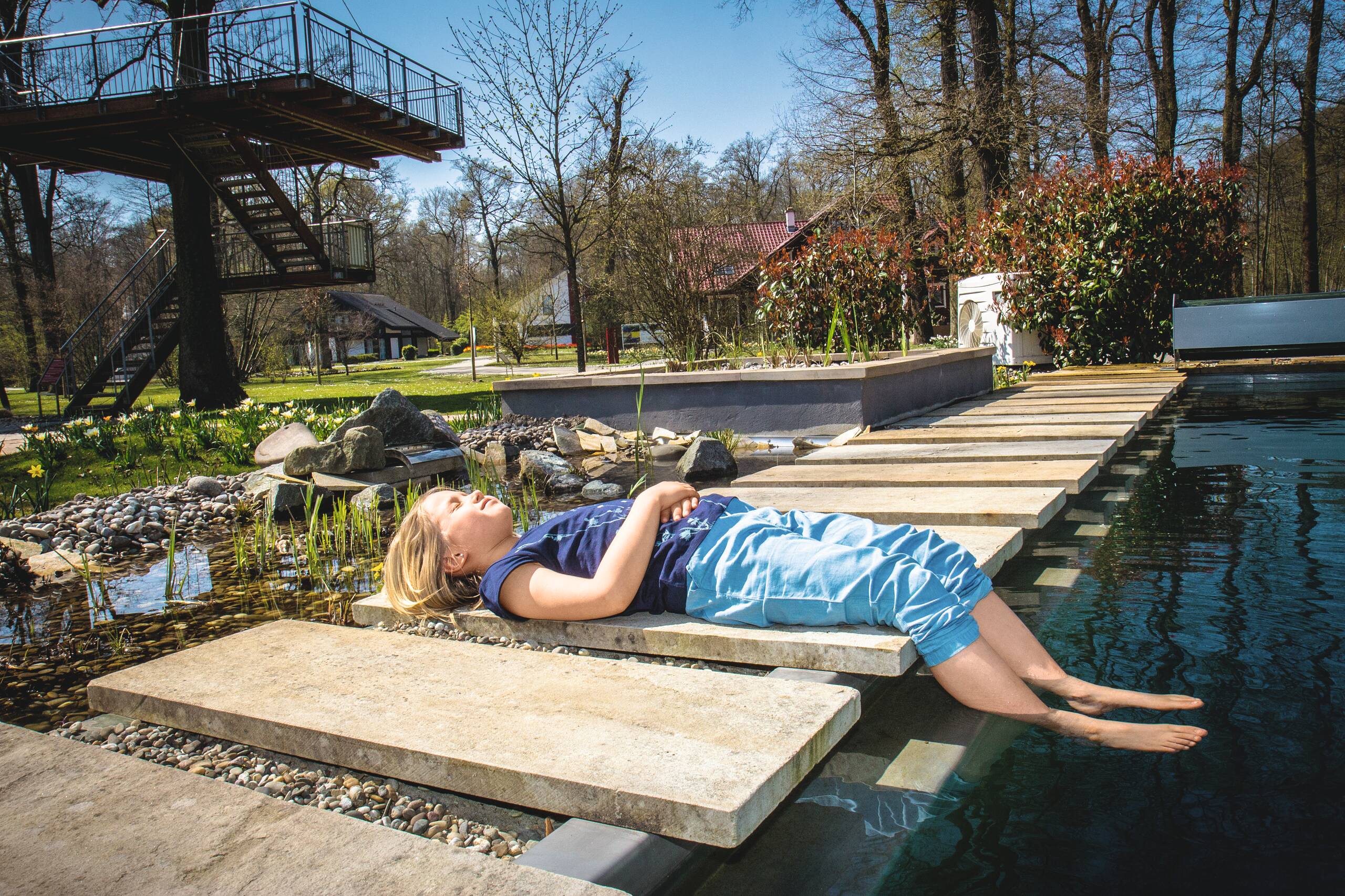 Kind liegt am Pool mit den Füßen im Wasser