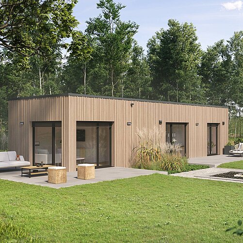 Ein modernes, eingeschossiges Holzhaus mit großen Fensterfronten ist umgeben von einem grünen Garten. Vor dem Haus stehen Sitzgelegenheiten und zwei kleine Tische aus Holz. Im Hintergrund sind Bäume und ein offenes, weites Gelände sichtbar.