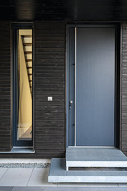 graue Haustür mit holzverkleideter Fassade